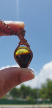 Load and play video in Gallery viewer, Natural Warm Yellow and Smoky Brown Coloured Baltic Amber Pear-shaped Cabochon Wire Wrapped Pendant
